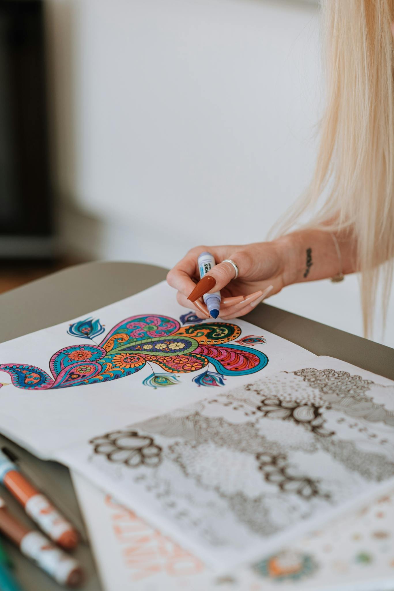 Woman coloring intricate patterns using markers, showcasing creativity and relaxation indoors.